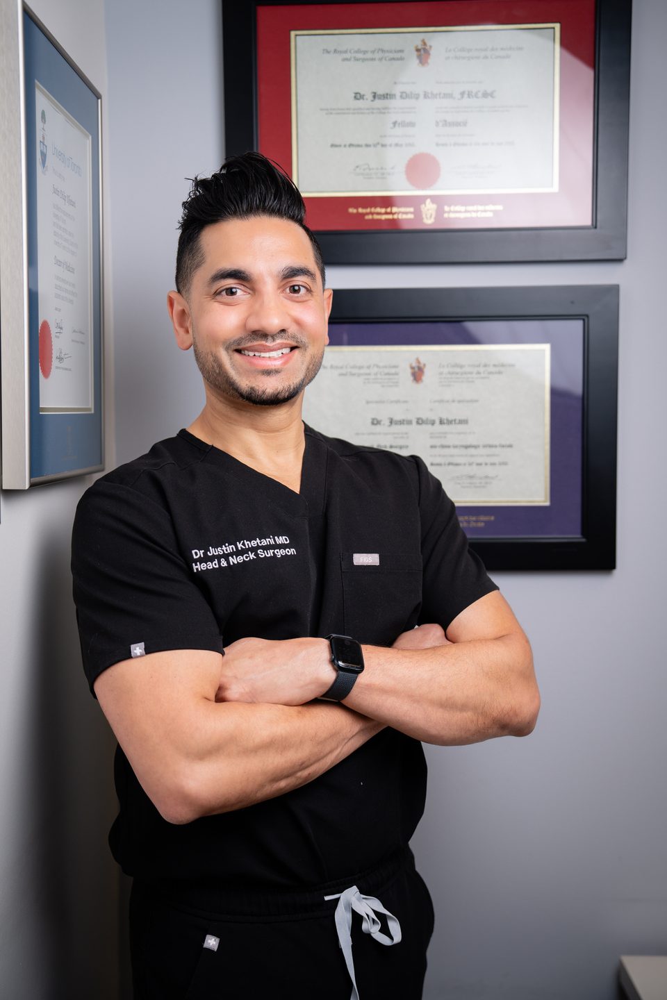 Dr. Justin Khetani standing beside his framed University of Toronto medical degree and Royal College of Physicians and Surgeons of Canada certificates