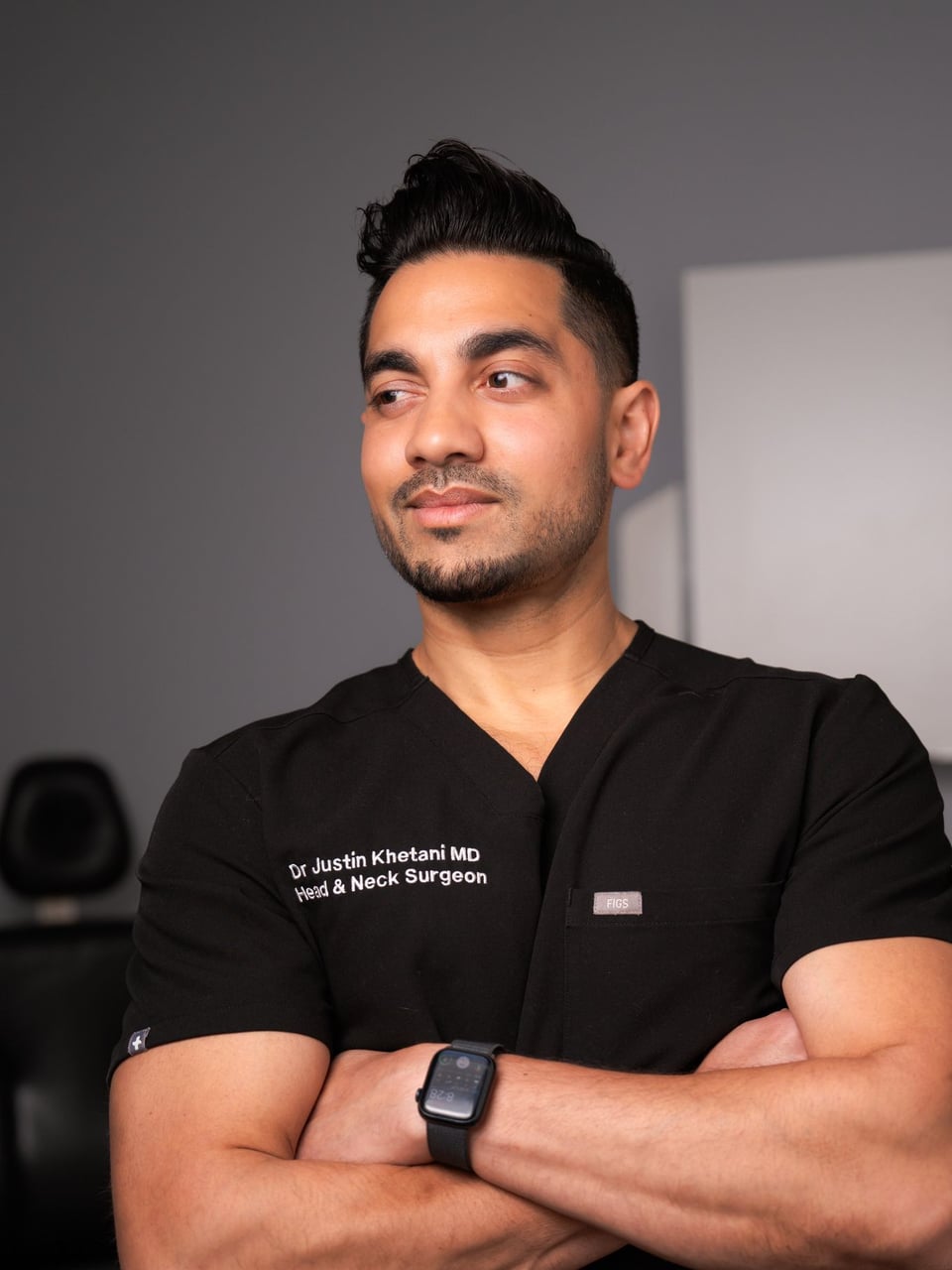 Dr. Justin Khetani, otolaryngologist and head and neck surgeon, standing with arms crossed in an examination room at his Burlington clinic